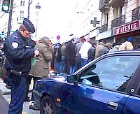 Policjant wypisuje mandat za złe parkowanie, a w tle nielegalne zgromadzenie.