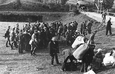 Wyrzuceni z domów Polacy, oczekują w punkcie zbornym na transport samochodowy (widoczny już na drugim planie) do obozu zbiorczego. Miejscowość Sól, przedpołudnie 24 września 1940 r. (fot. NSDAP; w zbiorach elektronicznych OKŚZpNP w Katowicach).
